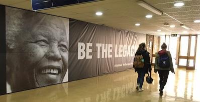 Students walk past the Nelson Mandela 100 memorial banner wall